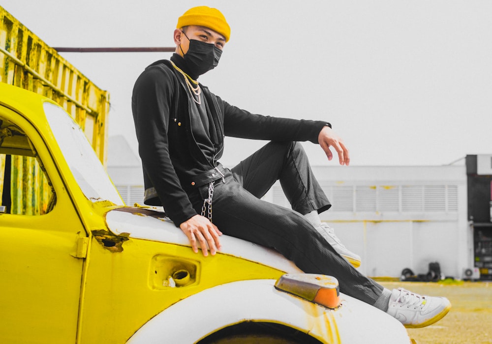 man in black jacket and black pants sitting on yellow car