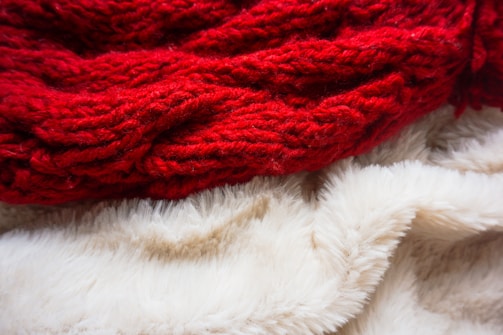 A close-up of a textured red knitted fabric resting on a soft, fluffy white fabric.