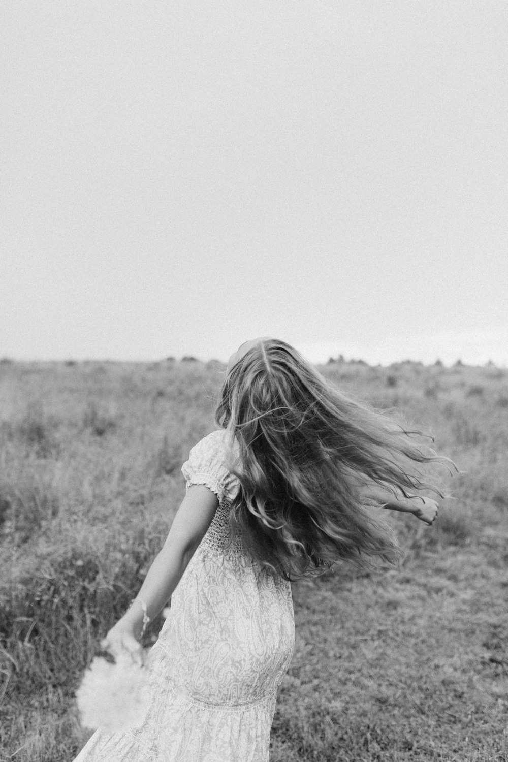 grayscale photo of woman in dress standing on grass field