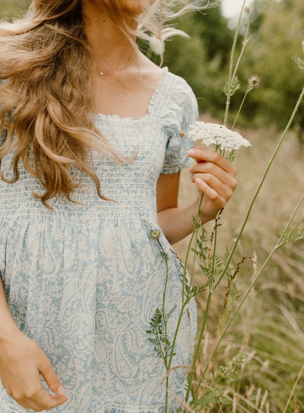 Femme en robe fleurie blanche tenant une fleur blanche