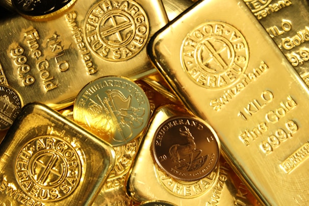 A collection of gold bars and coins, prominently displaying engravings such as '1 KILO Fine Gold 999.9' from Switzerland. The shiny surfaces reflect light, emphasizing the luxury and value associated with precious metals.