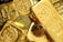 A collection of gold bars and coins, prominently displaying engravings such as '1 KILO Fine Gold 999.9' from Switzerland. The shiny surfaces reflect light, emphasizing the luxury and value associated with precious metals.