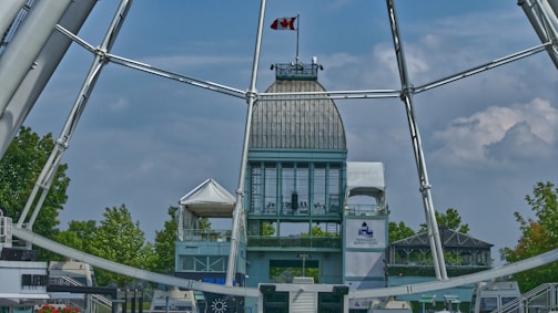 A tall building with a metal dome, featuring a Canadian flag on top, surrounded by trees and a large Ferris wheel structure.