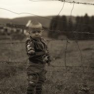 boy in brown and black camouflage jacket standing on green grass field during daytime