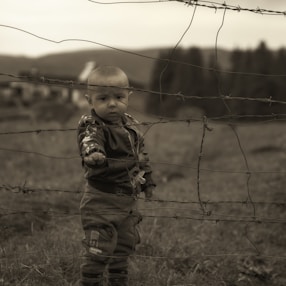 boy in brown and black camouflage jacket standing on green grass field during daytime