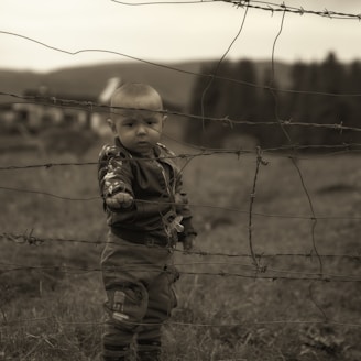 boy in brown and black camouflage jacket standing on green grass field during daytime