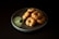 A plate of vadai, a type of savory Indian fritter, arranged neatly with a serving of green chutney on the side. The vadai are golden brown with visible herbs and spices, and the chutney appears creamy with a leaf garnish.