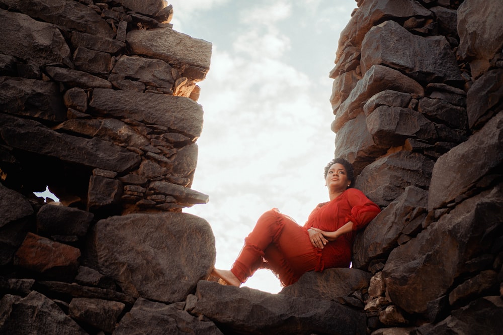 man in orange jacket sitting on brown rock formation during daytime