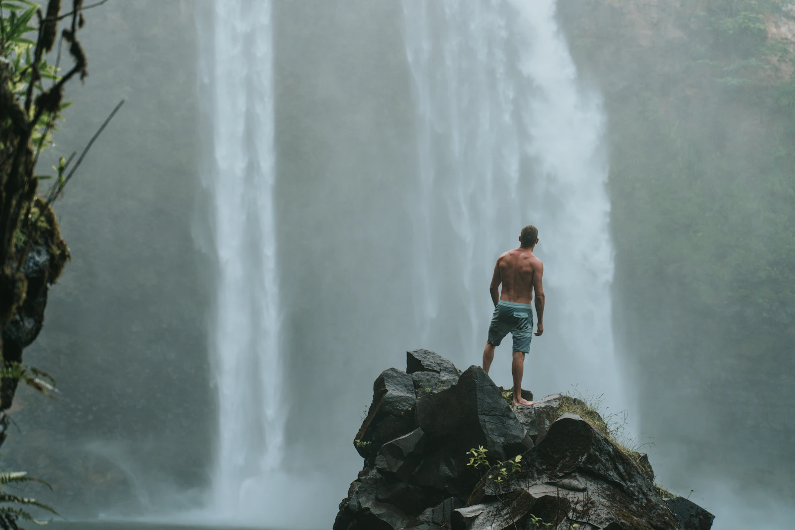 Excursionista de pie sobre una roca mojada en la base de una cascada en una ruta de senderismo en Kauai, Hawái