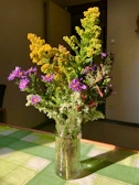 A vibrant yellow vase with fresh wildflowers sitting on a rustic windowsill.