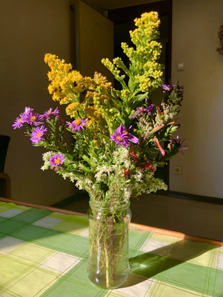 A bright yellow stoneware vase holding fresh wildflowers on a rustic windowsill.