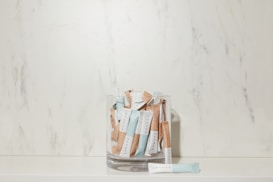 A glass container is filled with several sachets labeled 'SPRUCE' in a minimalist style, placed against a marble-textured backdrop. The sachets are predominantly blue and beige.