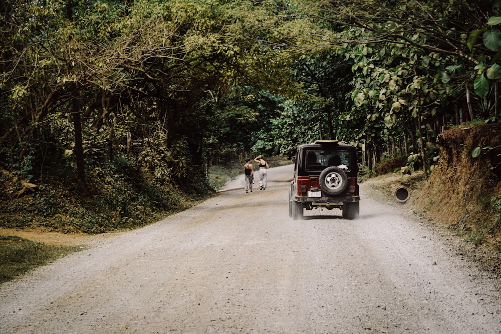 2 people standing beside red and black jeep wrangler on road during daytime