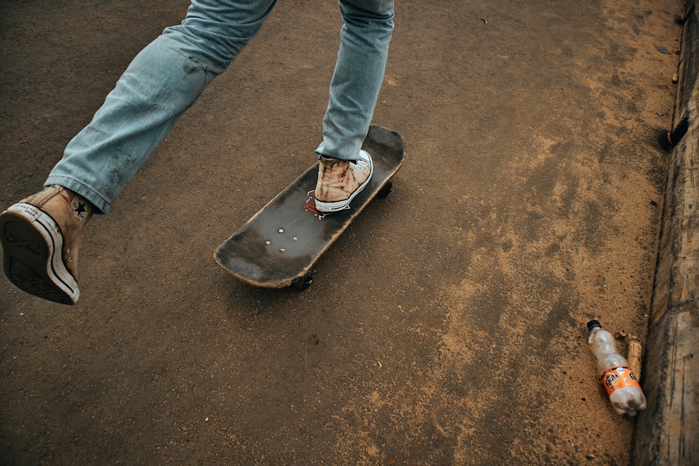 personne en jean denim bleu debout sur une planche à roulettes noire et rouge pendant la journée