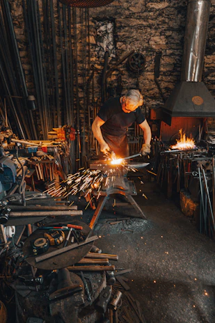 A skilled metalworker shaping a steel piece in a traditional workshop with modern tools.