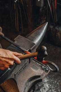persona che tiene in mano un martello che forgia su un incudine un pezzo di ferro