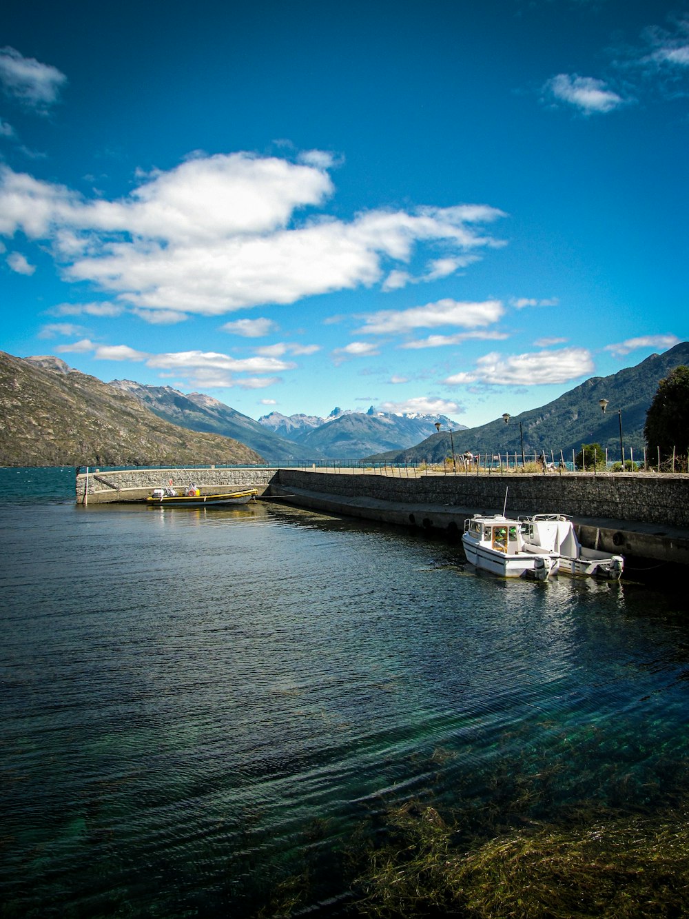 white boat on body of water near mountain under blue sky during daytime