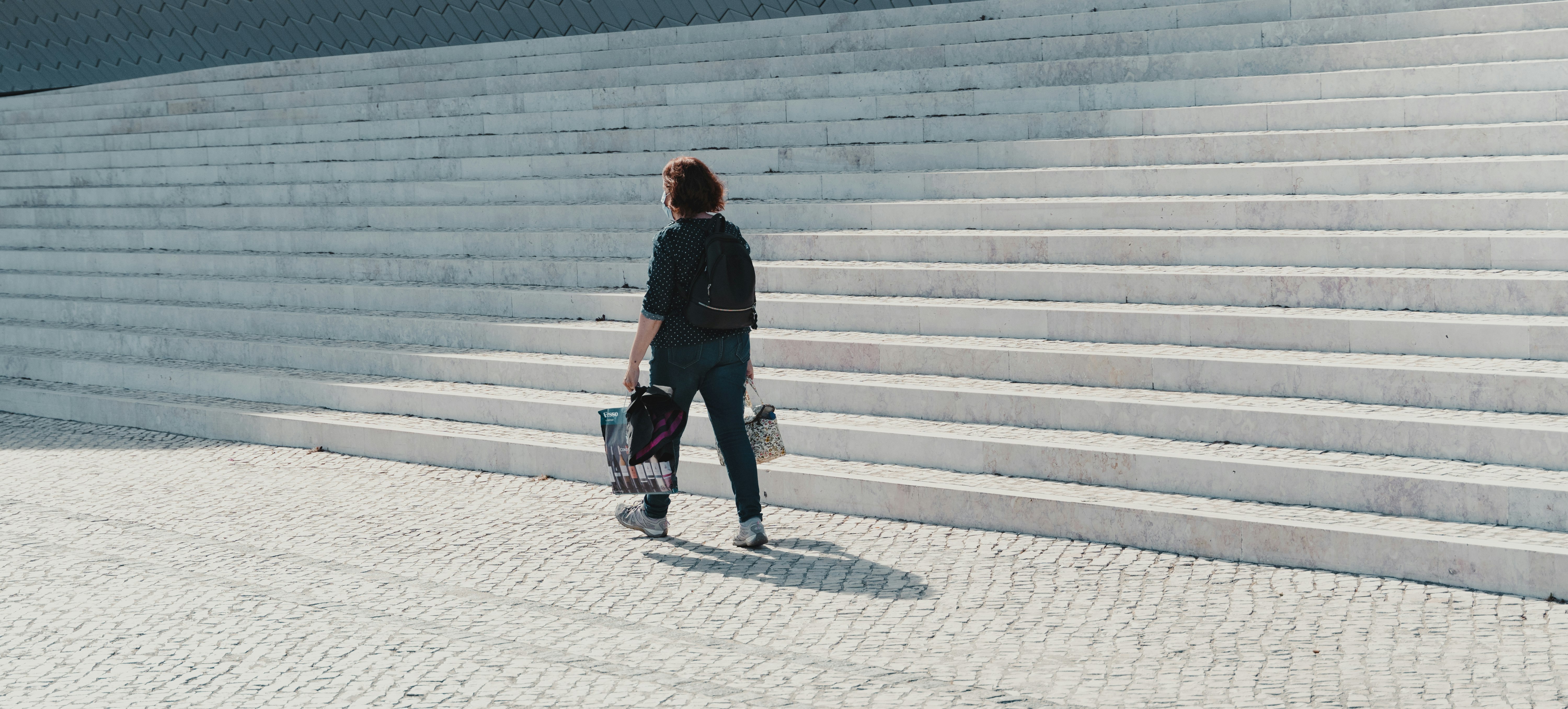 man in black jacket and blue denim jeans walking on sidewalk during daytime