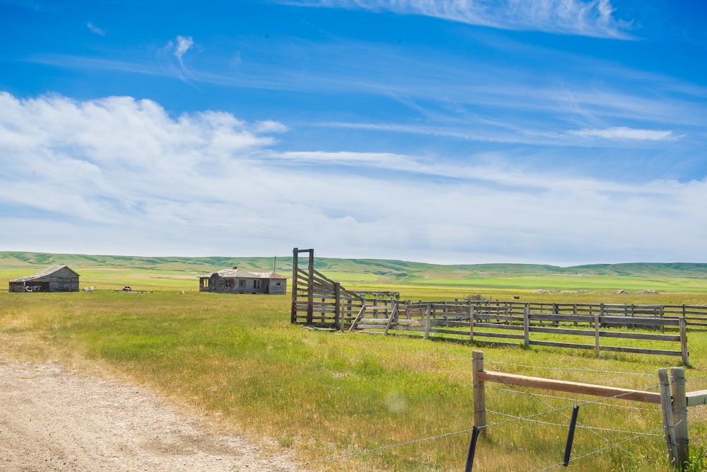 brown wooden fence on green grass field under blue sky and white clouds during daytime