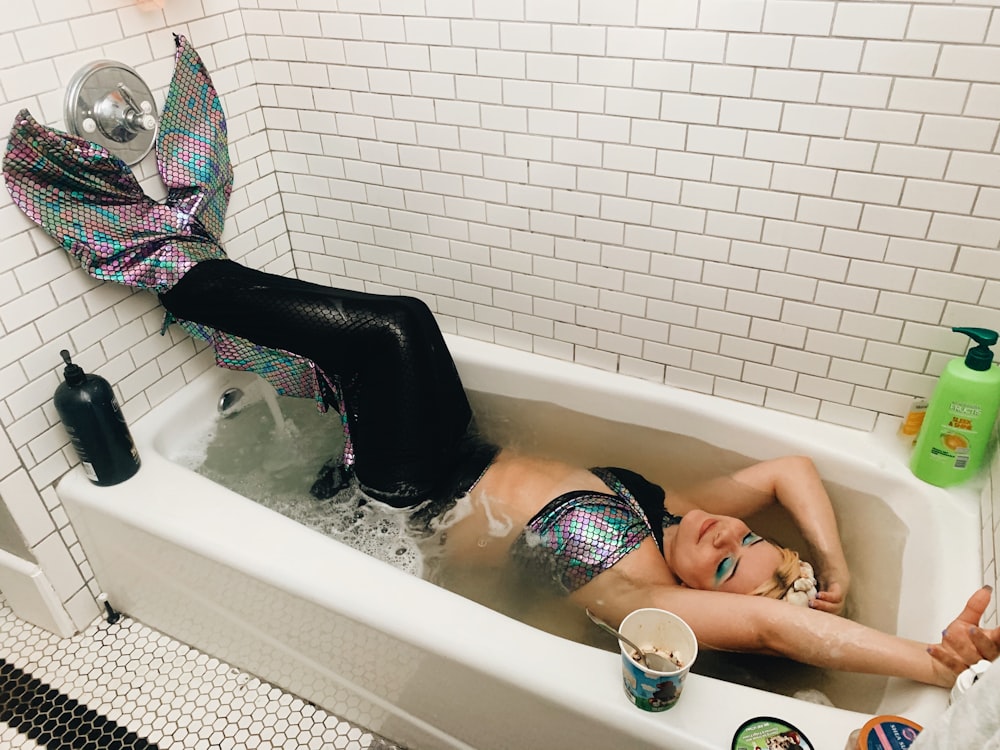 woman in black and white bikini lying on white ceramic bathtub