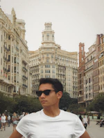 A person wearing square frame sunglasses while walking through a bustling city street.