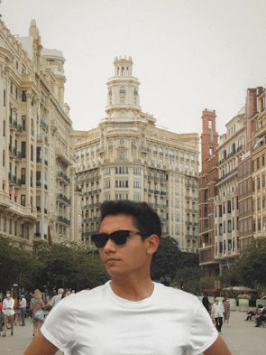 A person wearing square frame sunglasses while walking through a bustling city street.