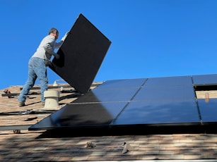 man in white dress shirt and blue denim jeans sitting on white and black solar panel