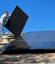 man in white dress shirt and blue denim jeans sitting on white and black solar panel