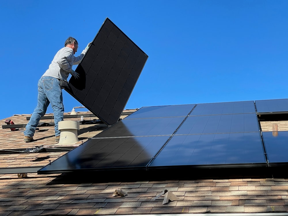 homme en chemise blanche et jean bleu assis sur un panneau solaire blanc et noir