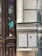 An urban street scene with two mosaic-style art pieces mounted on a worn wall. The artwork consists of white grid panels with scattered colorful squares and designs. Surrounding the art, the area is filled with graffiti on old wooden doors and a pole. The atmosphere is gritty and vibrant, with a mix of textures from the weathered surfaces and lively street art.