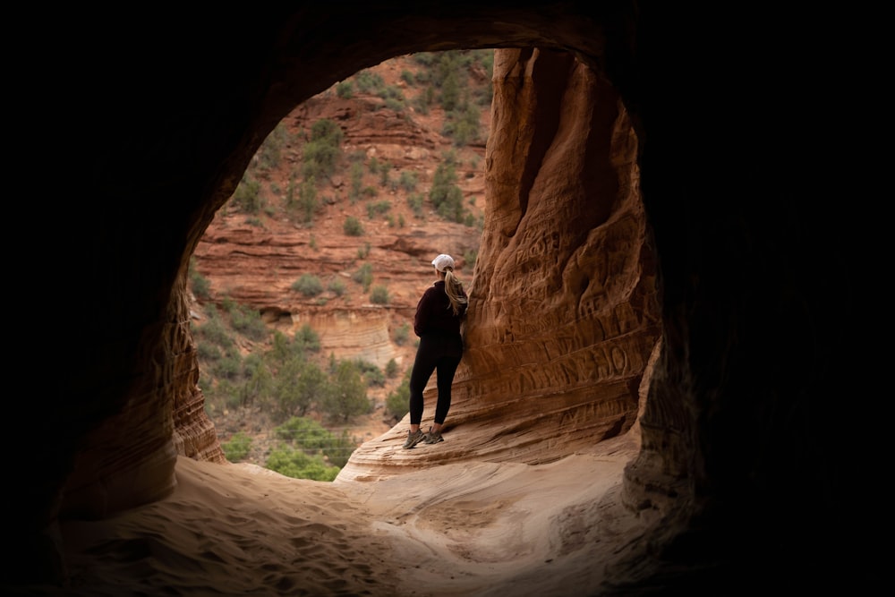 Hombre con chaqueta y pantalones negros de pie dentro de la cueva durante el día