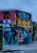A vibrant street mural featuring a variety of colorful elements, including a person with sunglasses and a red dress lounging, a silhouette of a person on a bicycle, fruit patterns, palm trees, and architectural elements. The mural is located on the corner of a building and includes text reading 'Wynwood Walls 305'.