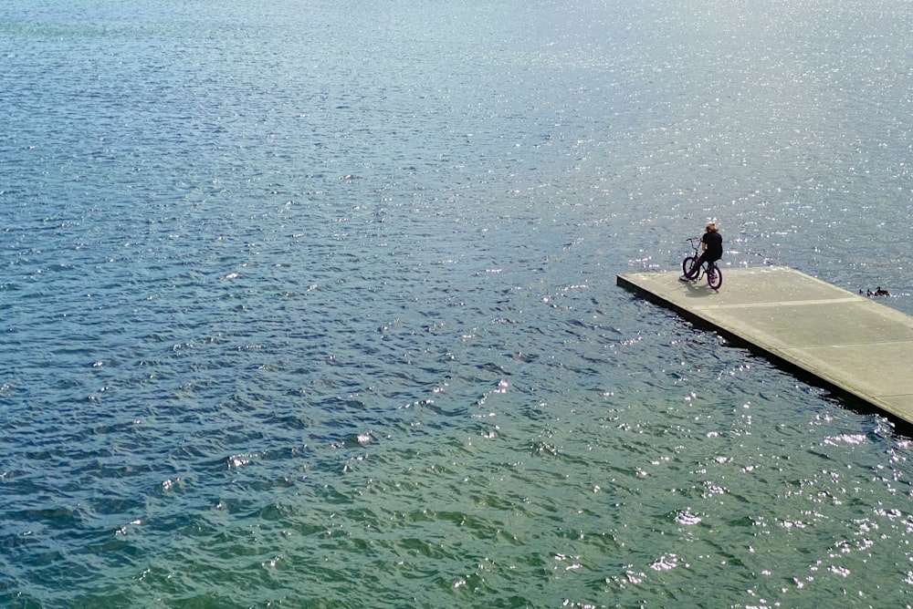 woman in black shirt sitting on brown wooden dock during daytime