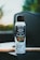 A can of Kirkland brand canola oil cooking spray placed on a dark surface. The can has a white body with a black cap, and the label features a photo of vegetables being cooked in a pan. The background is slightly blurred with hints of green and light colors, suggesting an outdoor setting with natural lighting.