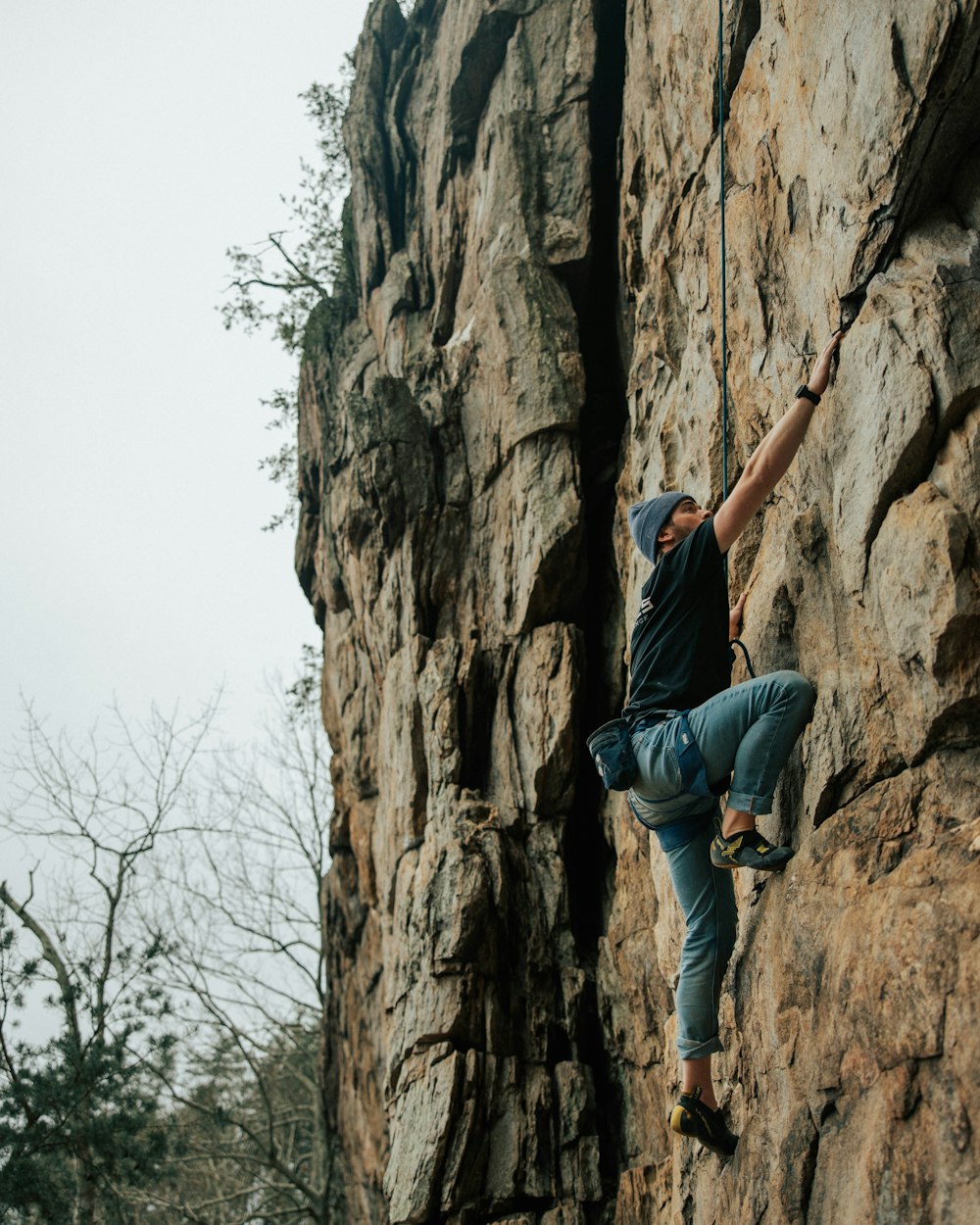 Mann in schwarzem T-Shirt und blauer Jeans klettert tagsüber auf braune Felsformation