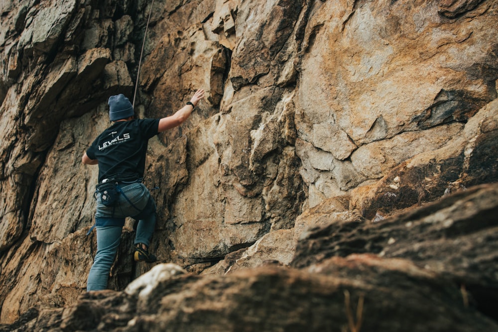 man in black t-shirt and blue denim jeans standing on rocky mountain during daytime