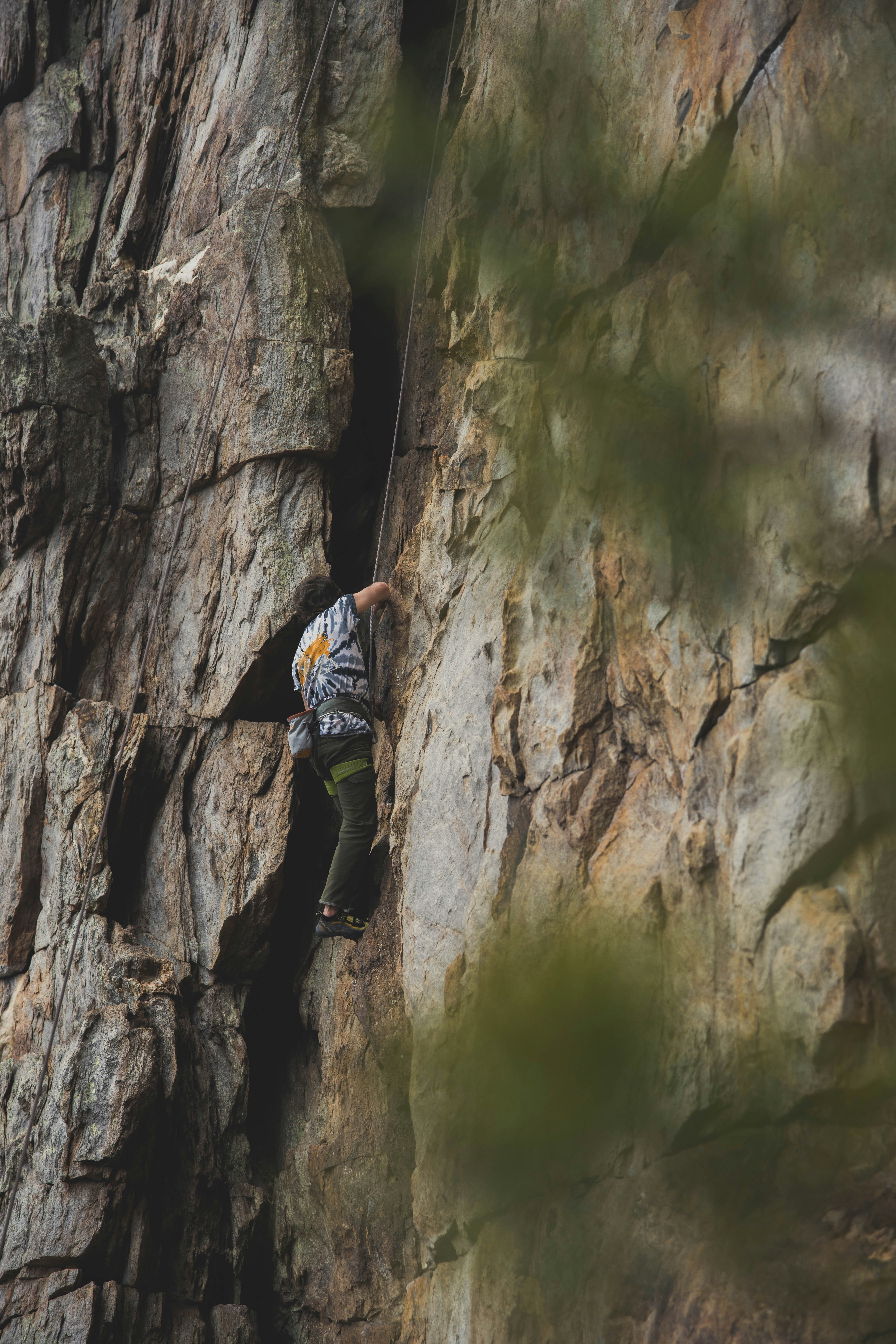Man in blue jacket climbing on brown rock formation during daytime