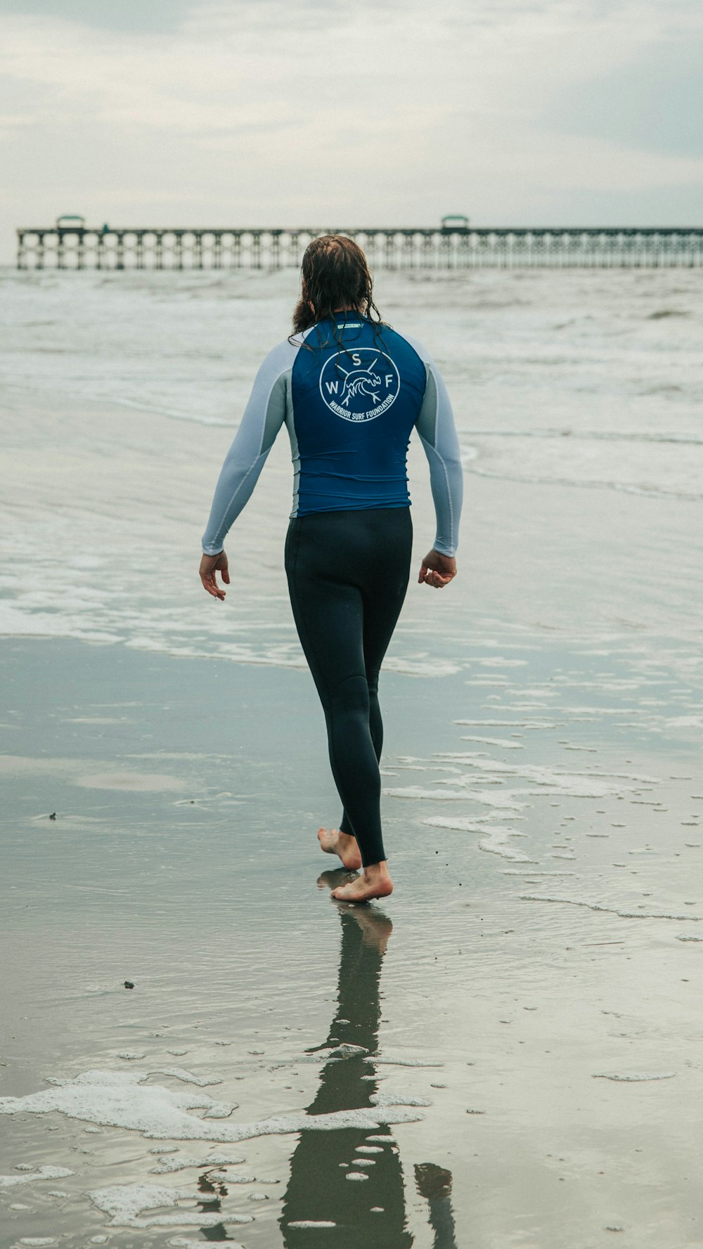 woman in blue and white long sleeve shirt and black leggings walking on beach during daytime