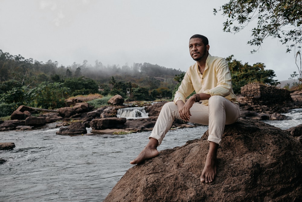 man in green dress shirt sitting on brown rock near river during daytime