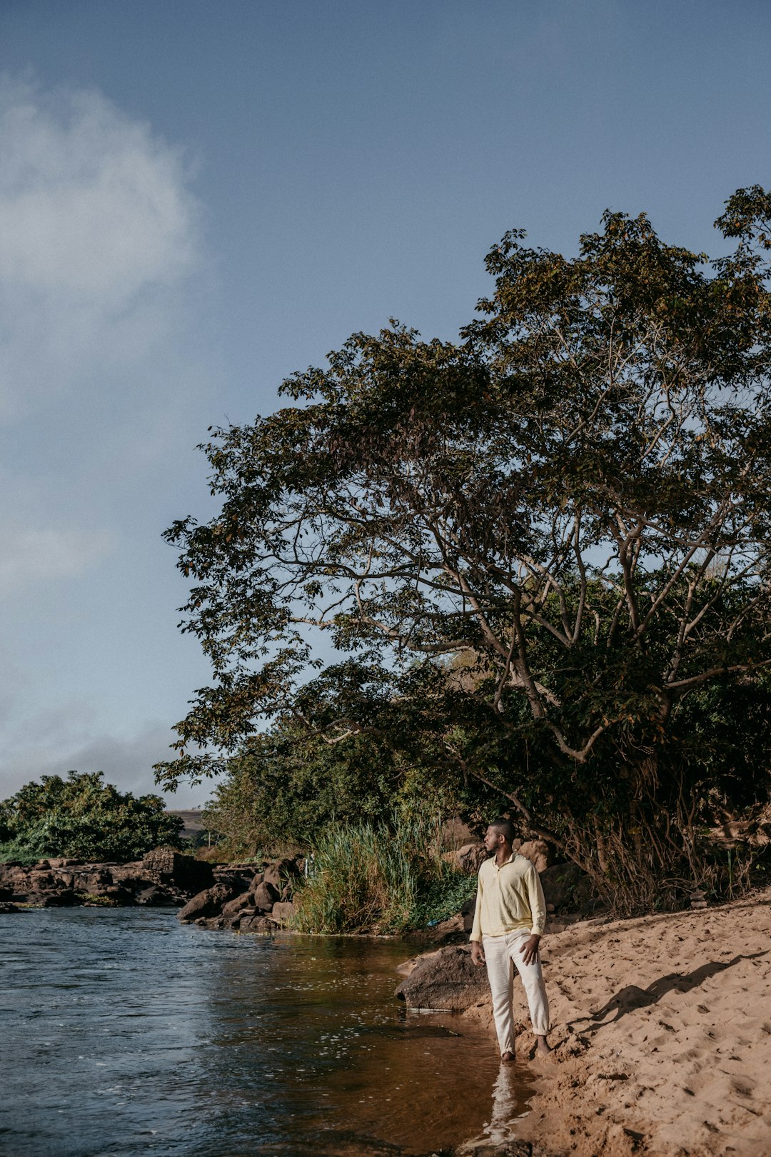 woman in white long sleeve shirt standing near green trees and body of water during daytime