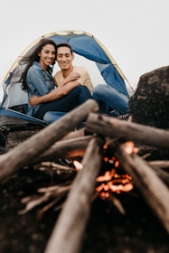 A smiling couple sharing travel stories around a campfire at dusk.