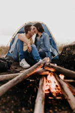 A couple enjoying a romantic moment by a campfire surrounded by nature.