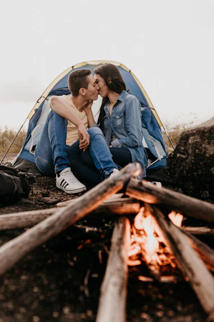A couple enjoying a romantic moment by a campfire surrounded by nature.
