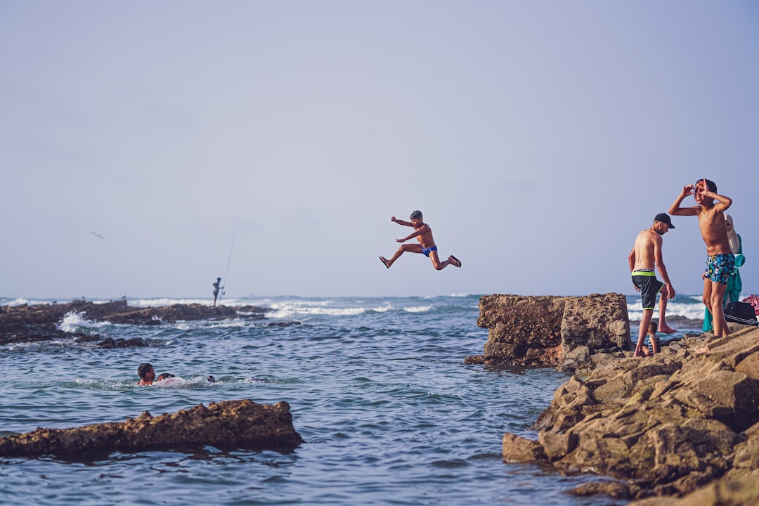 man in black shorts jumping on rocky shore during daytime