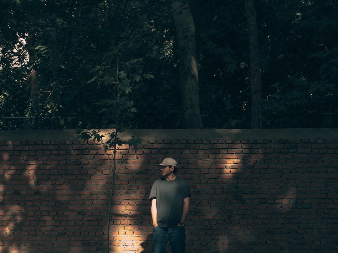 man in black tank top and blue denim shorts standing beside brown brick wall