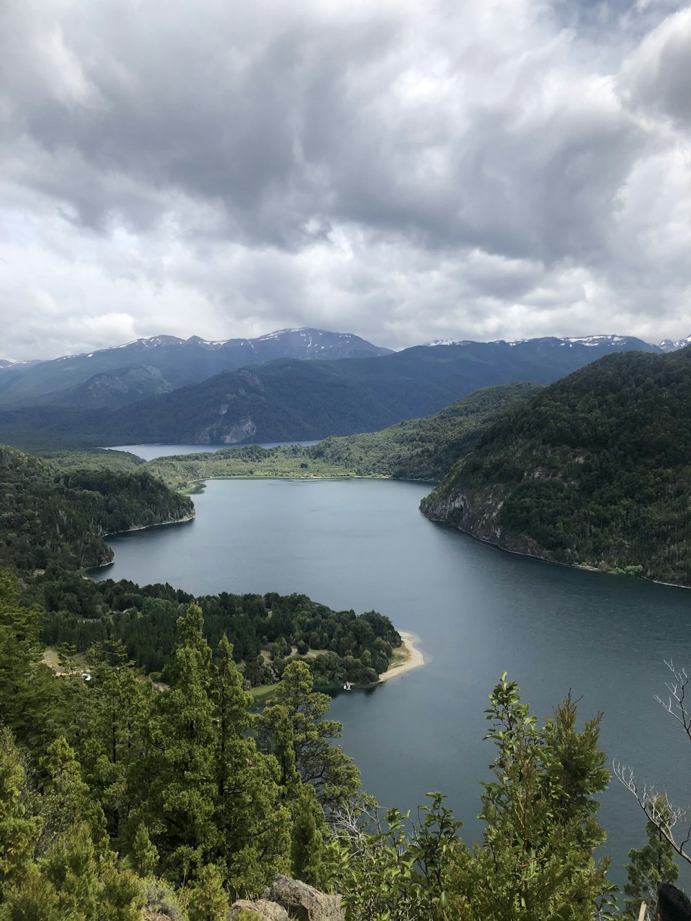 昼間の曇り空の下、川近くの緑の山々