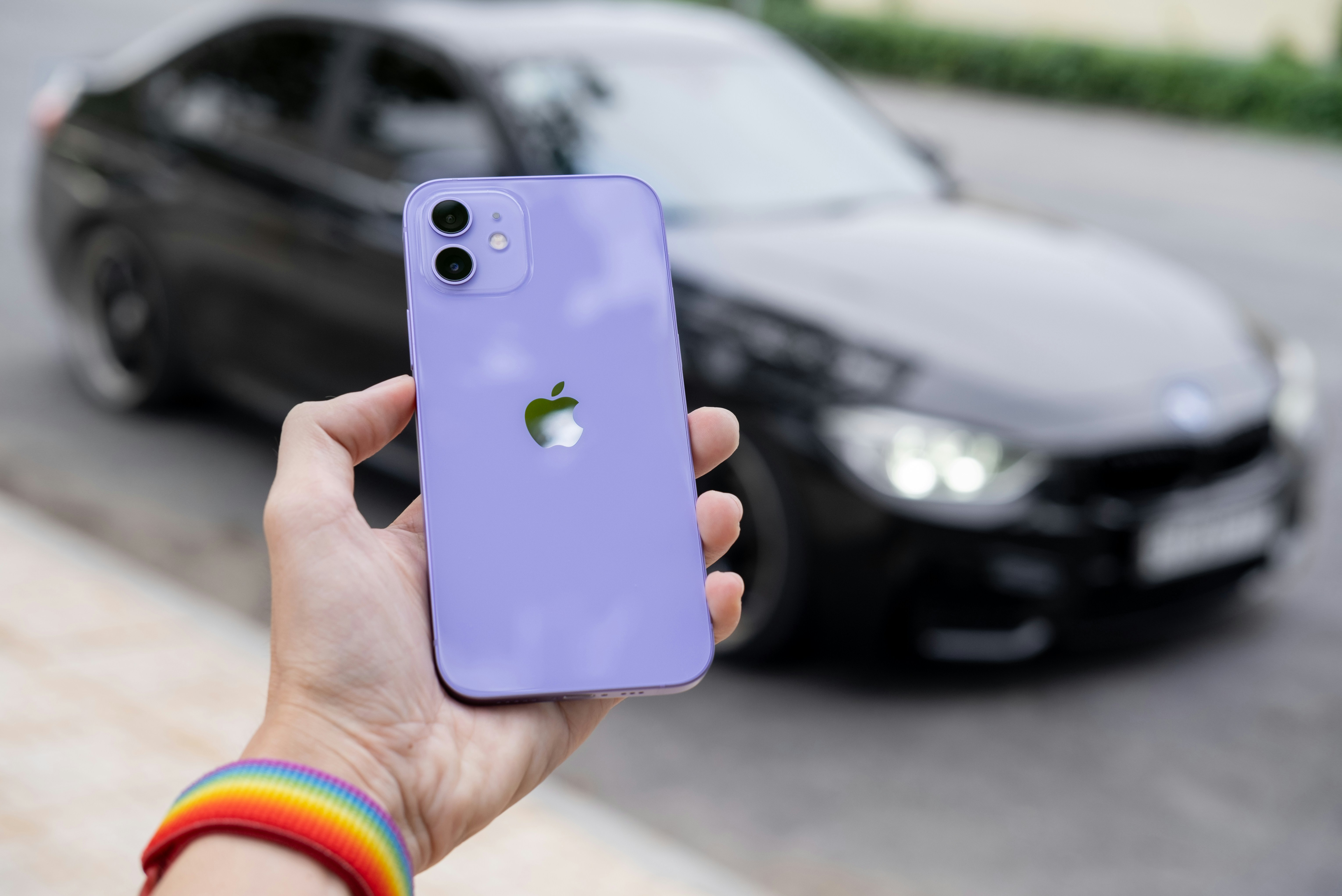 iPhone 14 in deep purple held in hand against blurred outdoor background