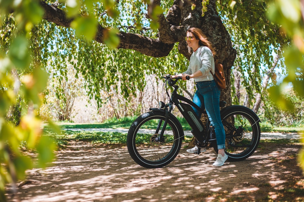 Mujer con camisa blanca y jeans de mezclilla azul montando bicicleta negra