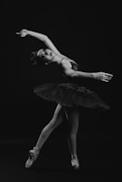 A ballerina is captured in mid-dance pose, wearing a classic tutu and ballet shoes. The image is in black and white, highlighting the graceful lines and elegance of her movement.