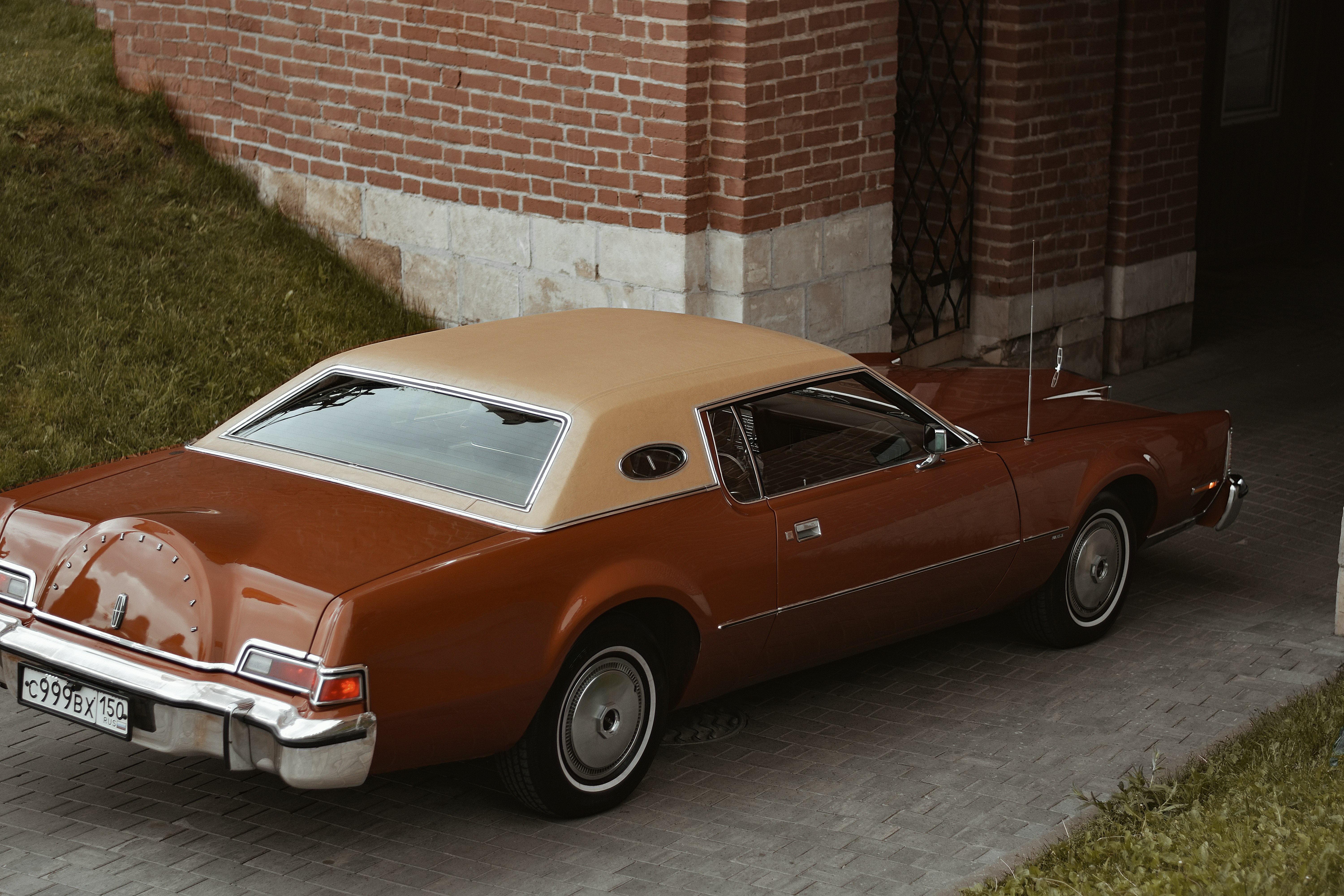 red and white sedan parked beside brown brick wall